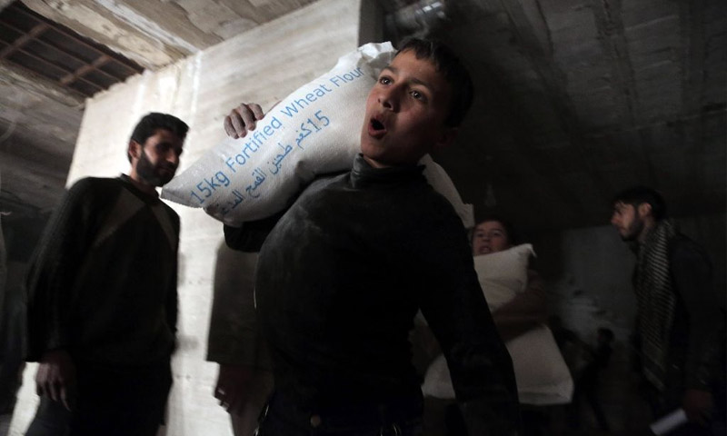 طفل يحمل كيس طحين في كفربطنا بريف دمشق (AFP)