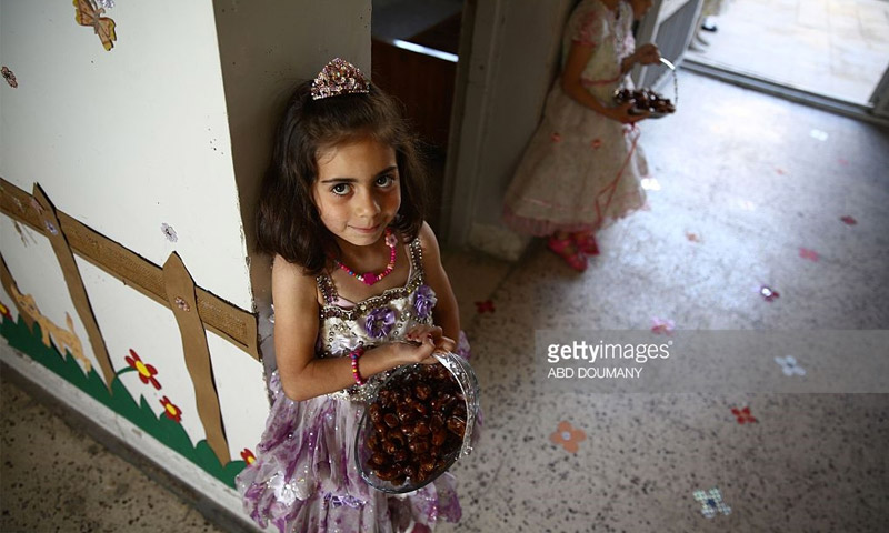 طفلة سورية تقدم التمور في احتفالٍ لمدرسة "سيف الدولة" في مدينة دوما - 25 أيار 2016 (عبد دوماني - AFP)