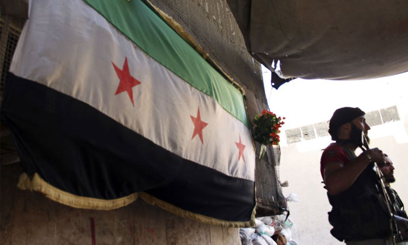 مقاتل من الجيش السوري الحر يقف أمام علم الجيش الحر- بستان القصر -حلب 2013 (رويترز)