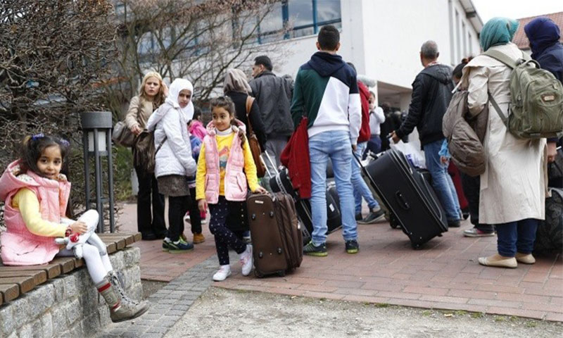 لاجئون سوريون أمام أحد مخيمات اللجوء في ألمانيا (رويترز)