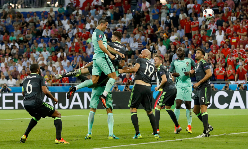 كريستيانور رونالدو أثناء توجيه كرة الهدف الأول للبرتغال والدفاع الويلزي يكتفي بالمشاهدة (رويترز)