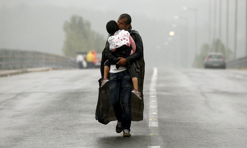لاجئ سوري يقبل ابنتها تحت المطر أثناء محاولة اجتياز الحدود اليونانية (رويترز)