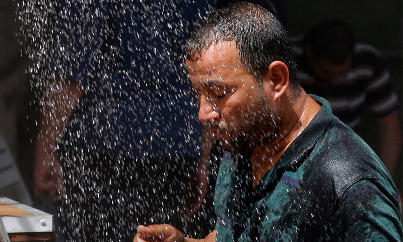 مواطن عراقي يتظلّل برذاذ ماء بسبب الحر (إنترنت)
