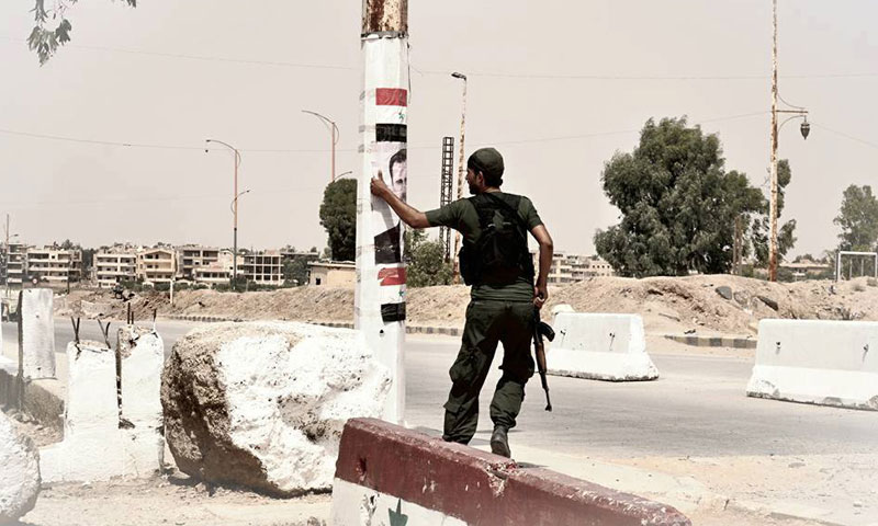مقاتل كردي يمزق صورة بشار الأسد من أمام فرع "الأمن الجنائي" في مدينة الحسكة- الاثنين 22 آب (تويتر)