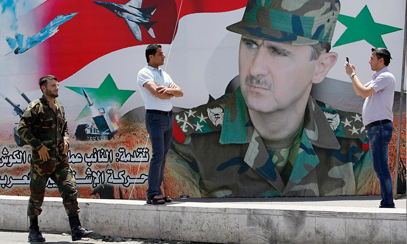 رجل يلتقط صورة بجانب لوحة لرئيس النظام السوري، بشار الأسد، في دمشق (رويترز)