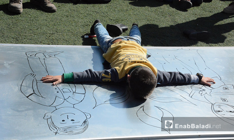 الطفل قاسم يحتضن رسمة خلال حفل داخل مخيم عطاء في إدلب - 23 شباط 2017 (عنب بلدي)
