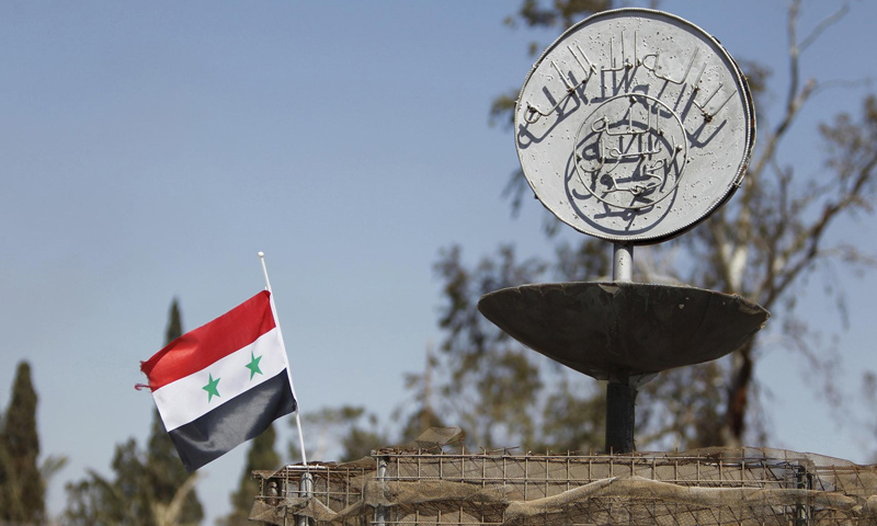 علم النظام السوري إلى جانب شعار لتنظيم "الدولة الإسلامية" في تدمر - 20 شباط 2017 (رويترز)