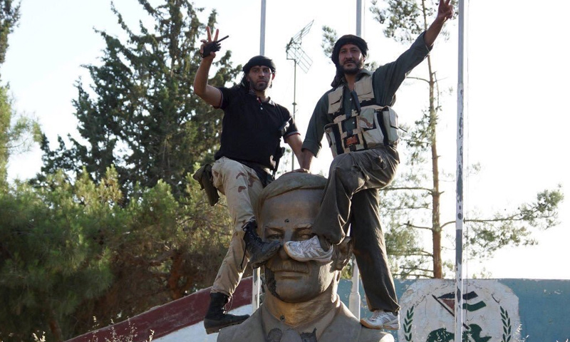 عناصر من الجيش الحر يضعون أقدامهم على تمثال حافظ الأسد في مدينة درعا - 21 حزيران 2015 - (رويترز)