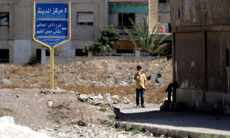 طفل يقف قرب لافتة طرقية في مركز مدينة حمص وسط سوريا - (رويترز)