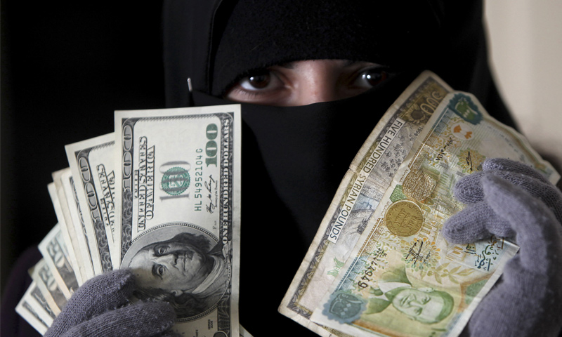 امرأة تحمل عملة سورية مقابل الدولار في العاصمة الأردنية عمان (رويترز)
