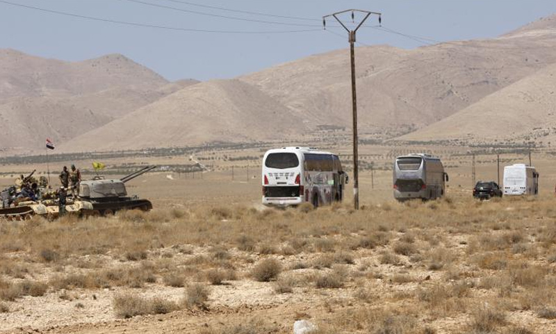 عناصر من قوات الأسد وحزب الله بجوار حافلات لتنظيم الدولة أثناء إخراجهم من القلمون - (انترنت)