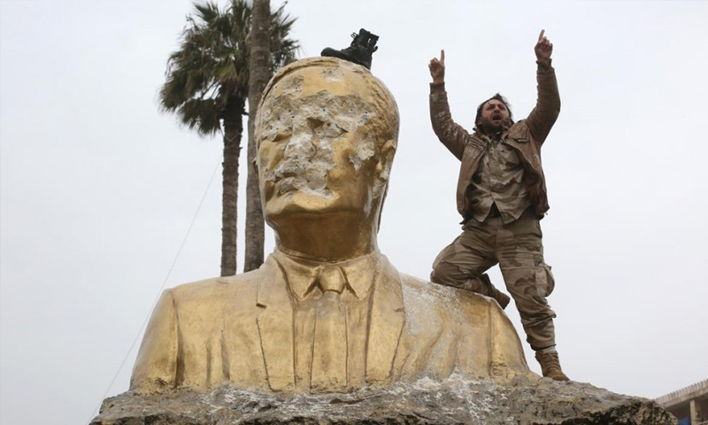 مقاتل من فصائل المعارضة إلى جانب تمثال حافظ الأسد بعد تحطيمه في إدلب - 28 آذار 2015 (ثائر حاج حمدان)