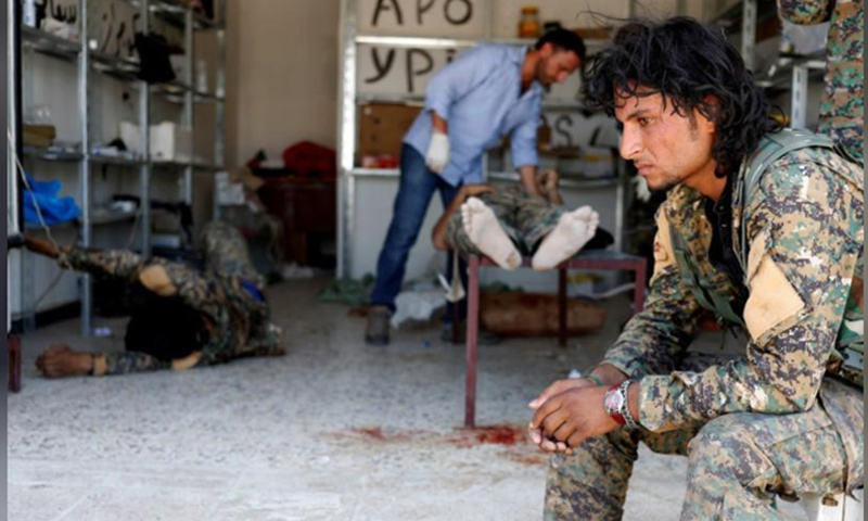 مقاتل من قوات سوريا الديمقراطية يجلس بينما يتلقى رفاقه علاجًا في مستشفى ميداني في الرقة- 28 حزيران 2017 (رويترز)