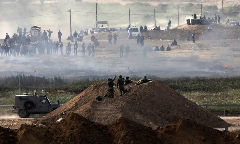 جنود إسرائيليون قرب السياج الأمني بينما محتجون على الجانب الآخر في قطاع غزة 5 نيسان 2018(رويترز)
