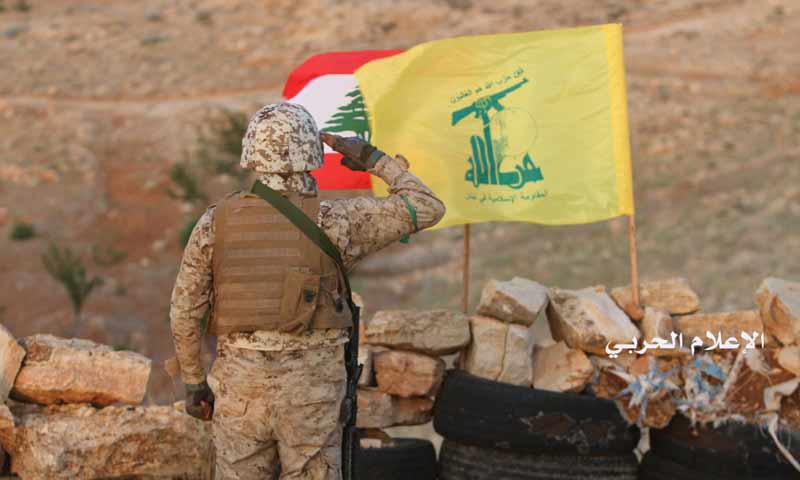مقاتل من حزب الله اللبناني أمام العلم اللبناني وراية الحزب جنوبي لبنان (الاعلام الحربي)