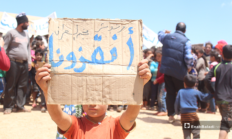 طفل يحمل لافتة كرتونية كتب عليها "أنقذونا" خلال مظاهرة لنازحي مخيم العمران غربي حربونش- 10 من أيار (عنب بلدي)