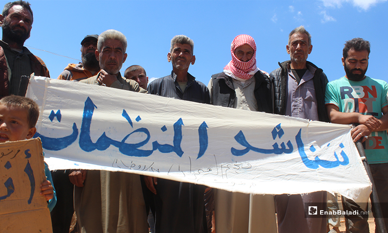 نازحو مخيم "العمران" غربي حربنوش يرفعون لافتة "نناشد المنظمات" خلال مظاهرتهم المطالبة بتوفيرالغذاء والماء والخبز والخدمات- 10 من أيار (عنب بلدي)