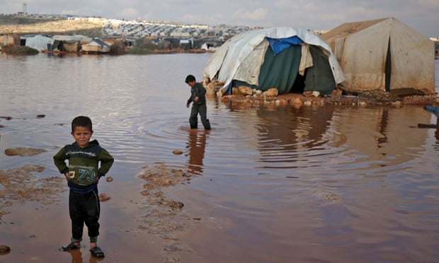 أطفال يلعبون بين الخيام التي غمرتها المياه في مخيم للنازحين السوريين بالقرب من بلدة كفرلوسين في إدلب. 26 من آذار 2021 (AFP)