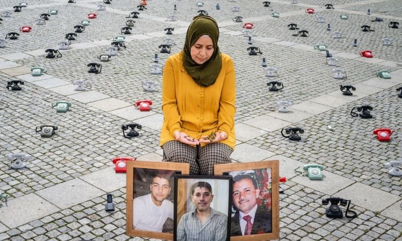 الناشطة السورية آمنة خولاني تجلس أمام صور أخوتها الثلاثة المعتقلين خلال وقفة تضامنية في برلين - 28 آب 2021 (تعديل عنب بلدي)
