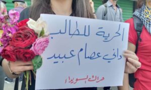لافتة رفعها محتجون في السويداء للمطالبة بالإفراج عن طالب جامعي معتقل لدى قوات النظام- 27 من نيسان 2024 (آرام نيوز)