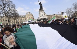متظاهرون يرفعون علم استقلال سوري كبيرًا الذكرى الرابعة لانطلاقة الثورة السورية في باريس – 14 آذار،  AFP
