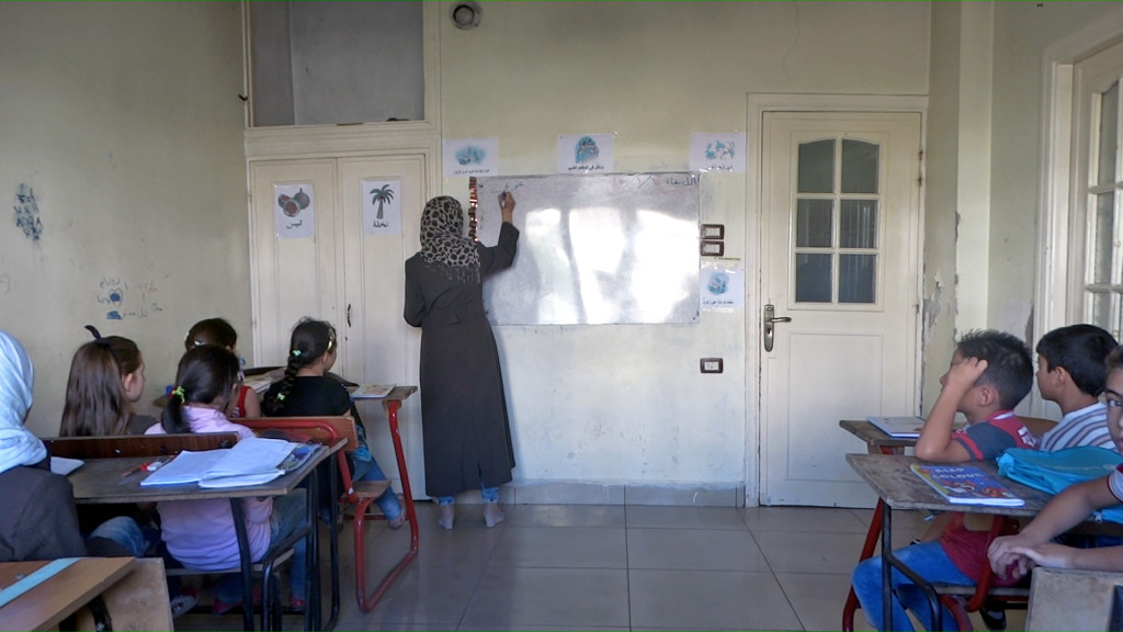 معلمة تشرح للطلاب في منزلها الذي حولته إلى مدرسة في حي الوعر الحمصي (عنب بلدي)