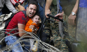 لاجئ سوري في ايدوميني شمال اليونان بينما تمنعه الشرطة من الوصول إلى محطة القطارات (AP)