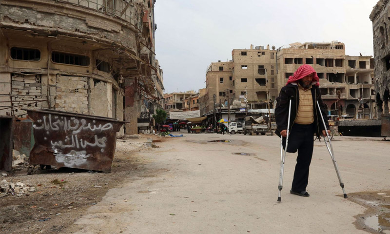 رجل مصاب في غوطة دمشق الشرقية يمشي بجانب حاوية عليها عبارة ساخرة في غوطة دمشق الشرقية - 13 نيسان 2016 (عامر الموهباني - AFP)