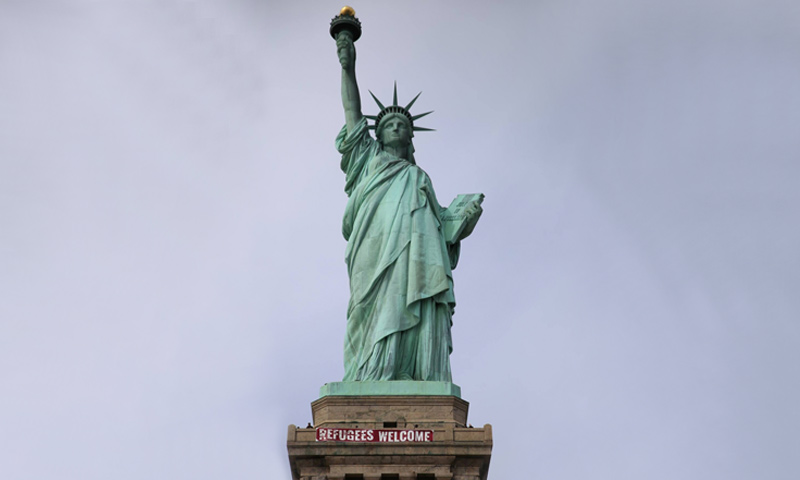 ناشطون يعلقون لافتة "أهلًا باللاجئين" على تمثال الحرية في نيويورك - الثلاثاء 21 شباط - (وكالات)