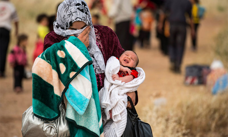 لاجئة سورية تحمل طفلها الرضيع في مخيم الزعتري للاجئين السوريين بالأردن - الأمم المتحدة
