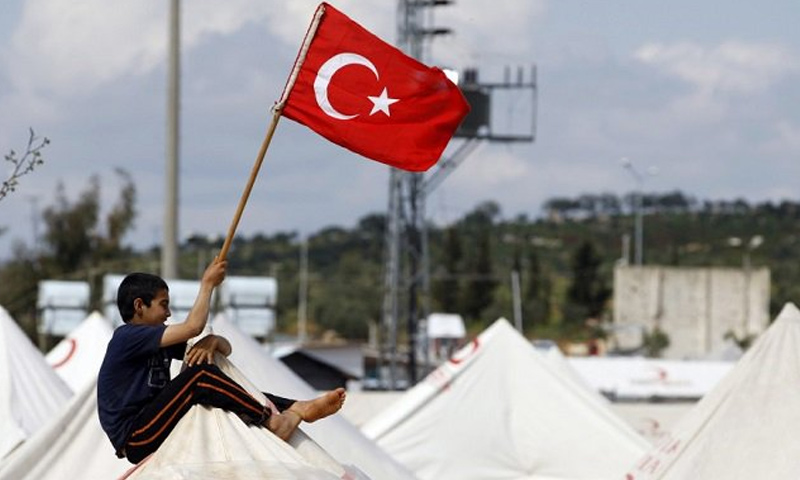 طفل سوري يرفع العلم التركي فوق خيمة في مراكز اللجوء على الأراضي التركية- (انترنت)