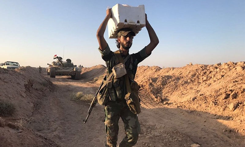 عنصر من قوات الأسد يحمل مواد غذائية أثناء العمليات العسسكرية في درير الزور - 15 أيلول 2017 - (سبوتنيك)

