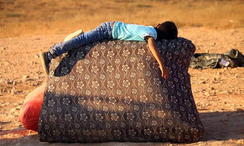 طفل يأخذ قسطًا من الراحة أثناء عودته مع عائلته إلى سوريا من الأردن - 29 آب 2017 (AFP)

