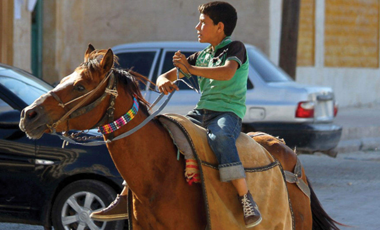 طفل سوري يقود حصانًا في مدينة إدلب بعد سماعه دوي غارة جوية - 18 تموز 2017( AFP)
