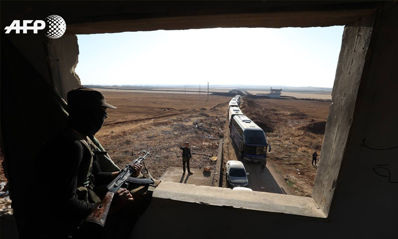 مقاتل من فصائل المعارضة ينظر إلى حافلات تقل مقاتلي بلدتي كفريا والفوعة - 19 من تموز 2018 (AFP عمر حاج قدور)
