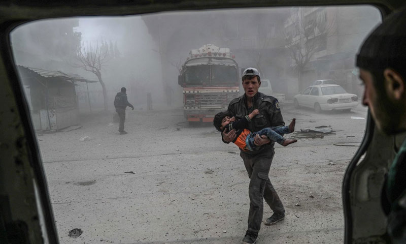 أحد عناصر الدفاع المدني يسعف الطفل في مدينة دوما بريف دمشق (epa)

