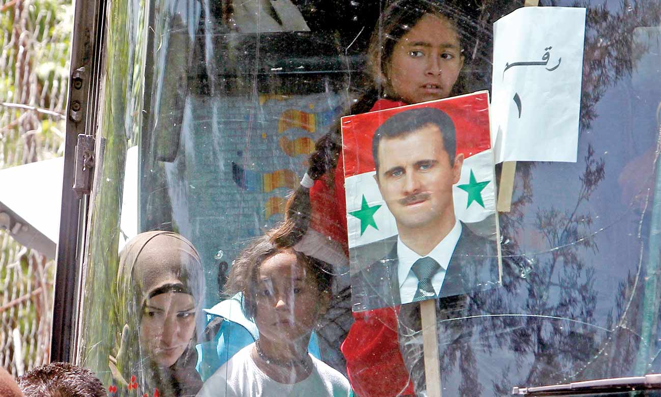 صورة رئيس النظام السوري بشار الأسد على متن حافلة تعود بللاجئون السوريون إلى سوريا - لبنان في 18 أبريل ، 2018 (رويترز)