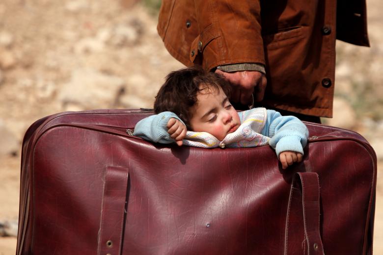 طفل ينام في حقيبة سفر بالقرب من بلدة بيت سوا في الغوطة الشرقية (رويترز)