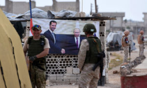 جنود روس يقفون بجانب صورة لرئيس النظام السوري بشار الأسد والرئيس الروسي فلاديمير بوتين في نقطة أبو ظهور بريف إدلب الشرقي - 1 حزيران 2018 (AFP)