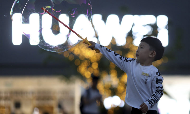 طفل يلعب بالفقاعات الصابونية أمام شعار شركة هواوي في بكين - 20 أيار 2019 (AP)