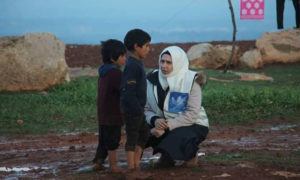 سيدة من فريق ياسمينات سوريات تتحدث مع طفلين في الشمال السوري (ياسمينات سوريات)

