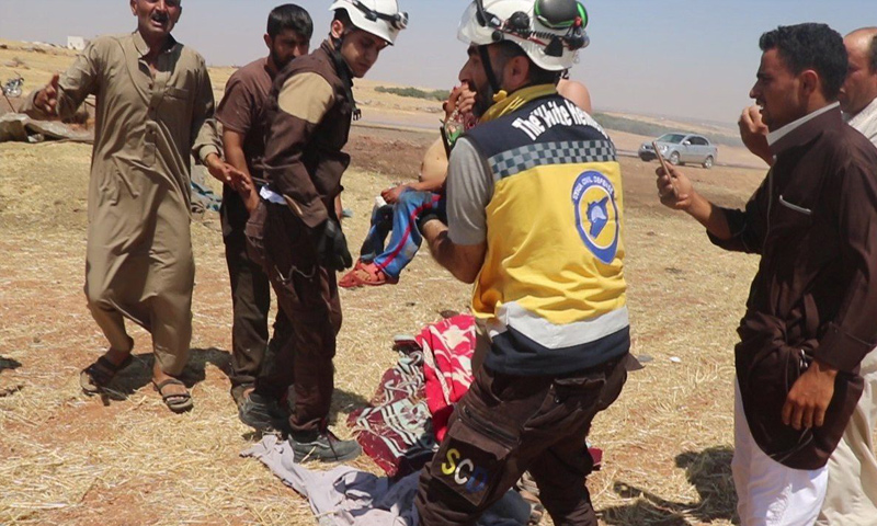 عنصر من الدفاع المدني يحمل طفلًا قتل جراء القصف الجوي على مخيم للنازحين في بلدة دير الشرقي بريف إدلب الشرقي - 9 من تموز 2019 (الدفاع المدني)