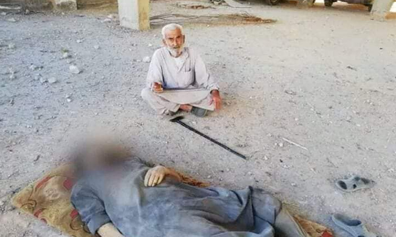 التسعيني قنبر البيوش يجلس قبالة جثمان ابنه نهاد في كفرنبل بريف إدلب - (فيس بوك)