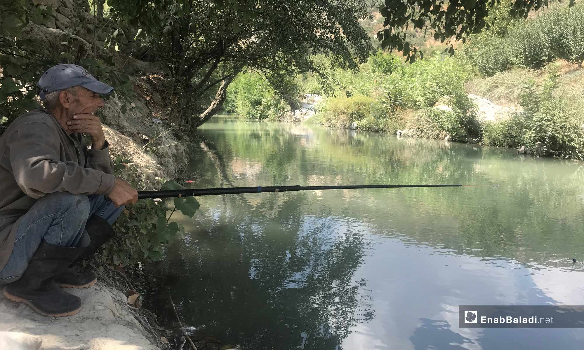 رجل يصطاد السمك على نهر العاصي قرب مدينة دركوش بريف إدلب الغربي- 8 من أيلول 2019 (عنب بلدي)