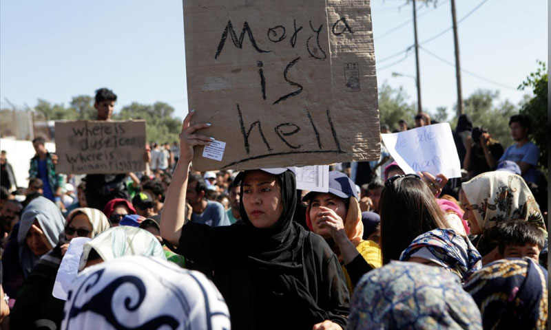 مهاجرة تحمل لافتة "موريا هي الجحيم" خلال احتجاجات على سوء الأوضاع المعيشية في المخيم المزدحم على جزيرة ليسبوس - 1 تشرين الأول 2019 (رويترز)