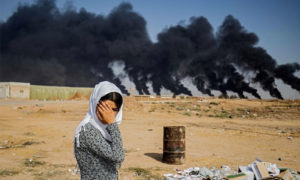 سيدة تغطي وجهها قرب تل تمر في محافظة الحسكة شمالي سوريا أمام دخان يتصاعد من قصف تركي في عملية 