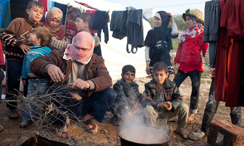 نازحون سوريون يطهون الطعام في مخيم قاح القريب من الحدود التركية (الأمم المتحدة)