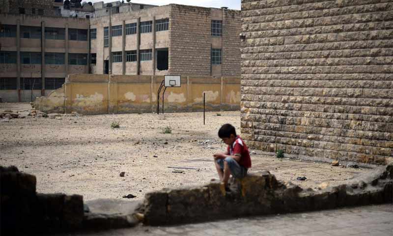 طفل سوري يجلس بجوار مدرسة تضررت جراء قصف النظام السوري لمدينة حلب - 2013 (AFP)