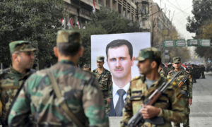  جنود سوريون يمرون أمام لوحة لرئيس النظام السوري بشار الأسد في ذكرى عام على سيطرة قواته على مدينة حلب - 21 كانون الأول 2017 (AFP)
