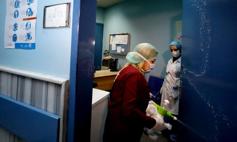 امرأة من العاملين بالرعاية الصحية تقوم بتعقيم باب في مستشفى بدمشق(رويترز)